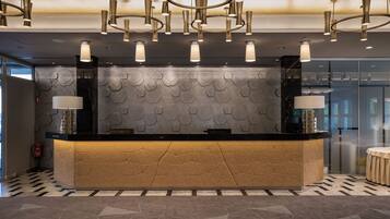 A reception area with a modern design, featuring a central counter with geometric patterns, ambient lighting, and a patterned wall in the background.
