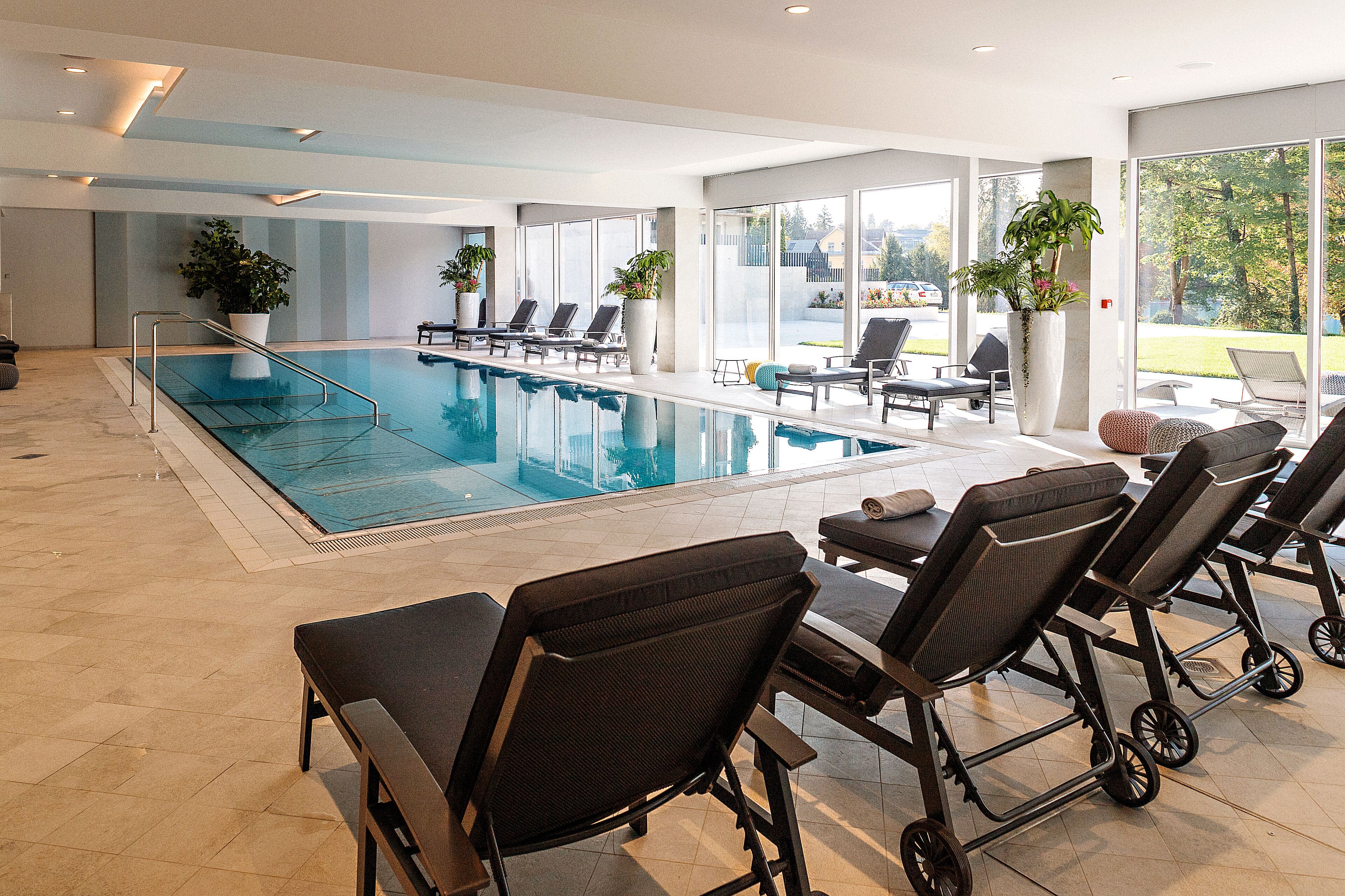 A modern indoor swimming pool with lounge chairs and potted plants.