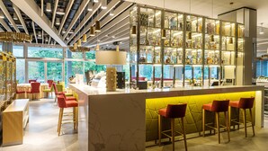 Zona de bar moderna con mostrador de mármol, taburetes rojos y un separador de vidrio que exhibe varios objetos.