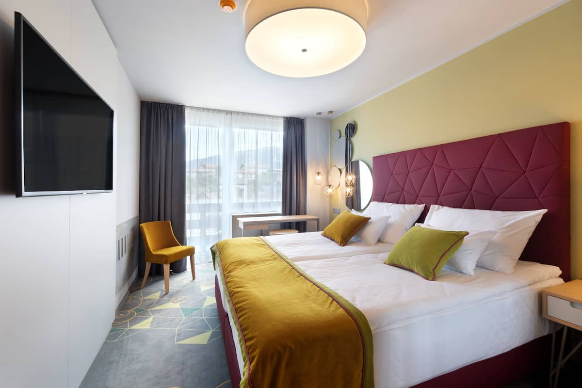 A hotel room with two beds, a TV, a desk, and a chair.