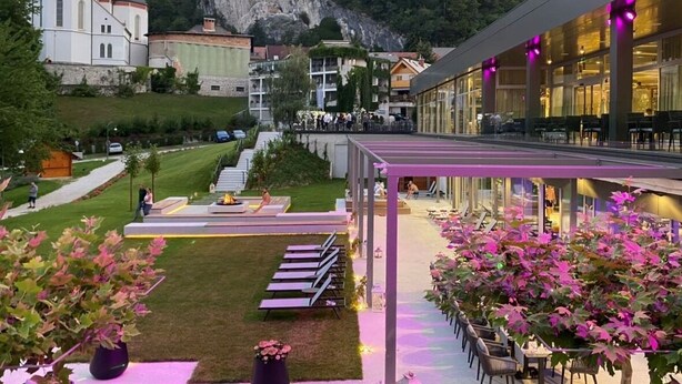 Un patio de hotel con mobiliario exterior, vistas a una iglesia y montañas al fondo.