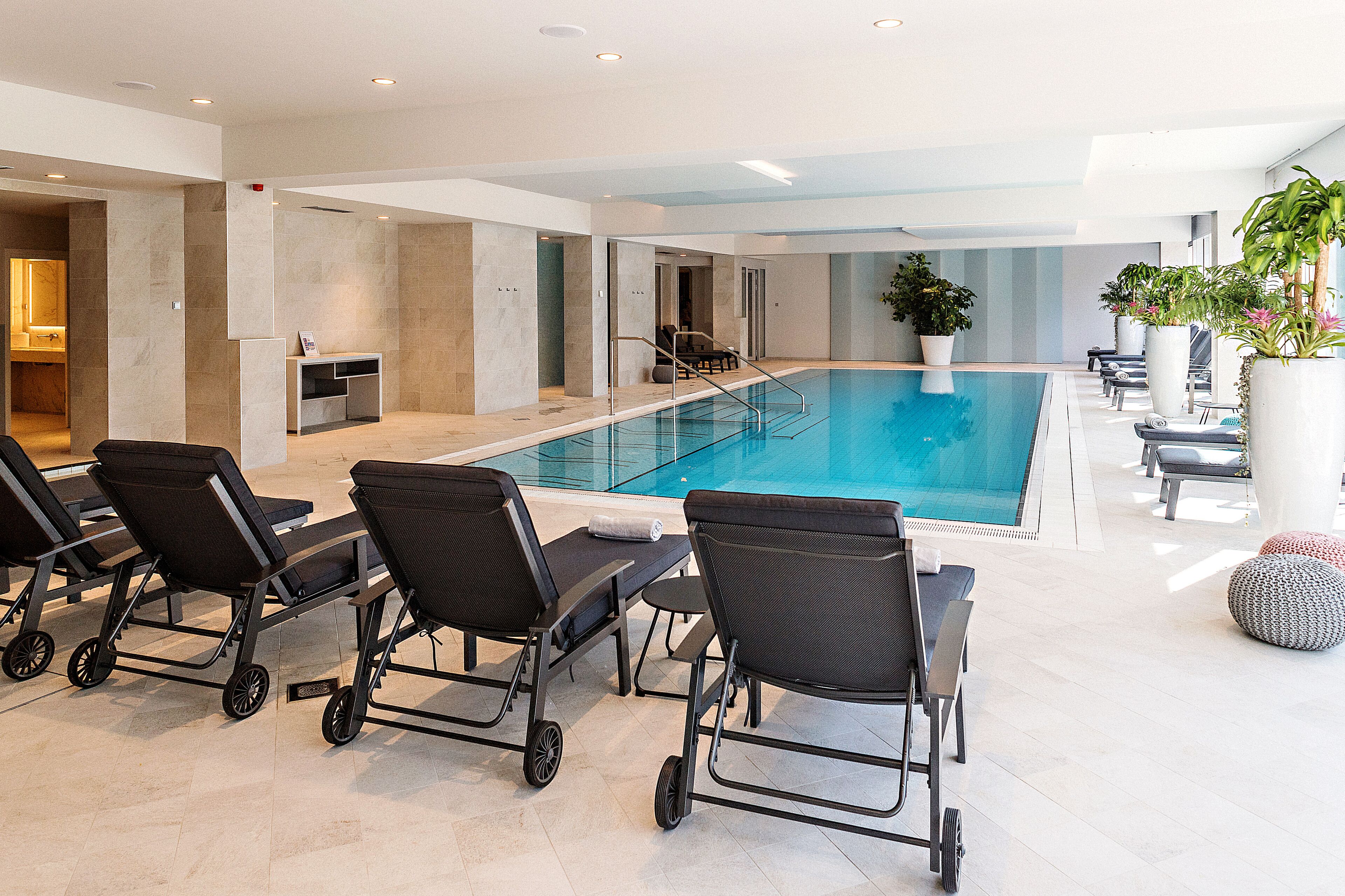 A modern indoor pool area with lounge chairs and a reception desk.