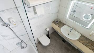 A modern bathroom with a glass-enclosed shower, a white toilet, a sink with a marble countertop, and a mirror with a built-in light.