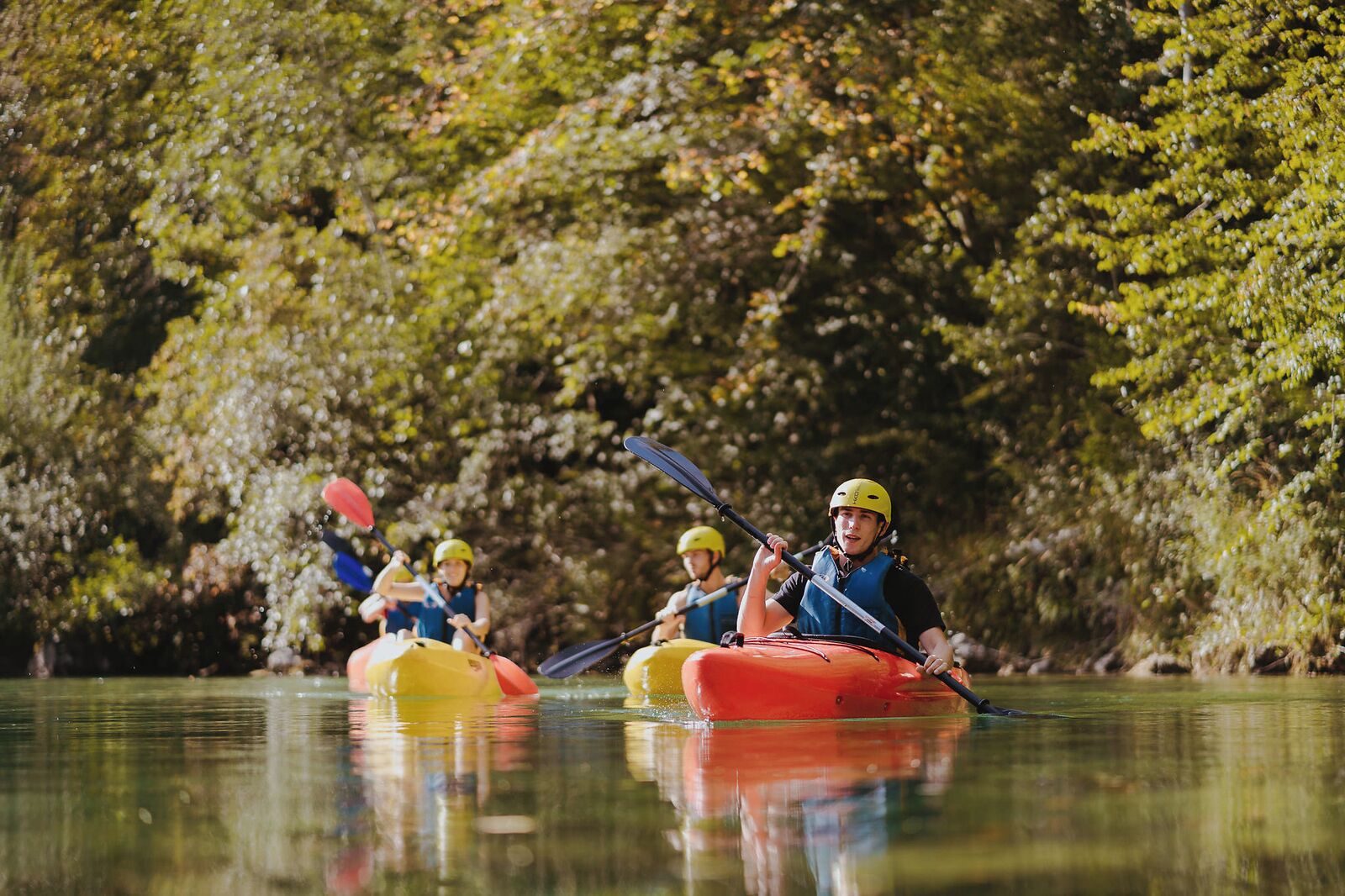 Un groupe de personnes pratiquant le kayak sur une rivière paisible, entourée d’une végétation luxuriante.