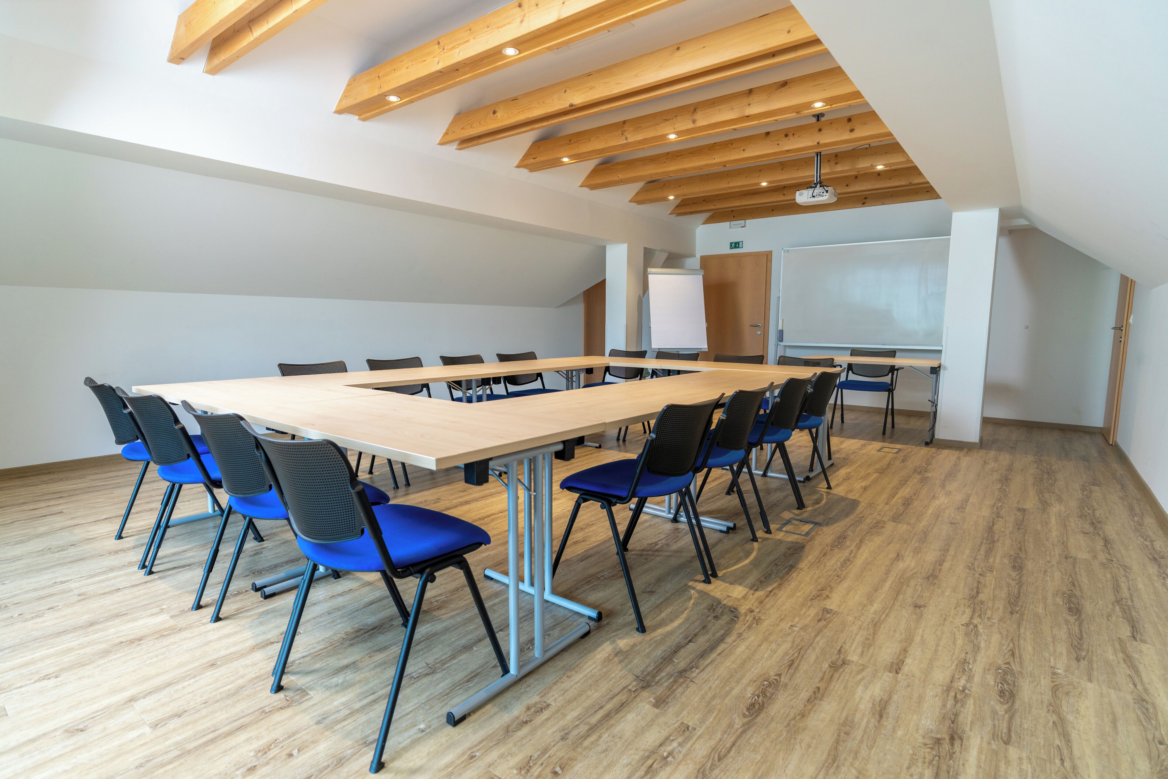 A conference room with a long table, blue chairs, wooden beams on the ceiling, and a whiteboard.