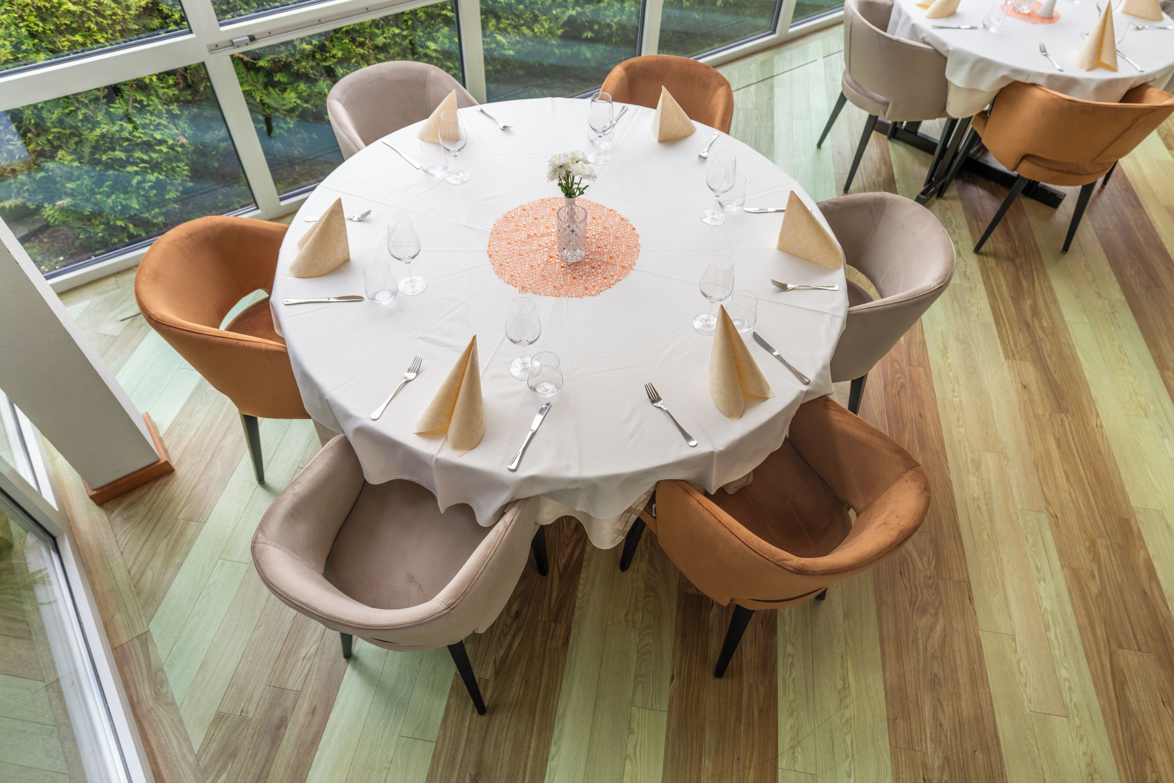 A round dining table with a white tablecloth, surrounded by six chairs with brown cushions.
