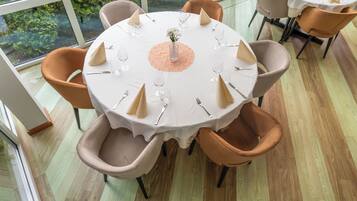 A round dining table with a white tablecloth, surrounded by six chairs with brown cushions.