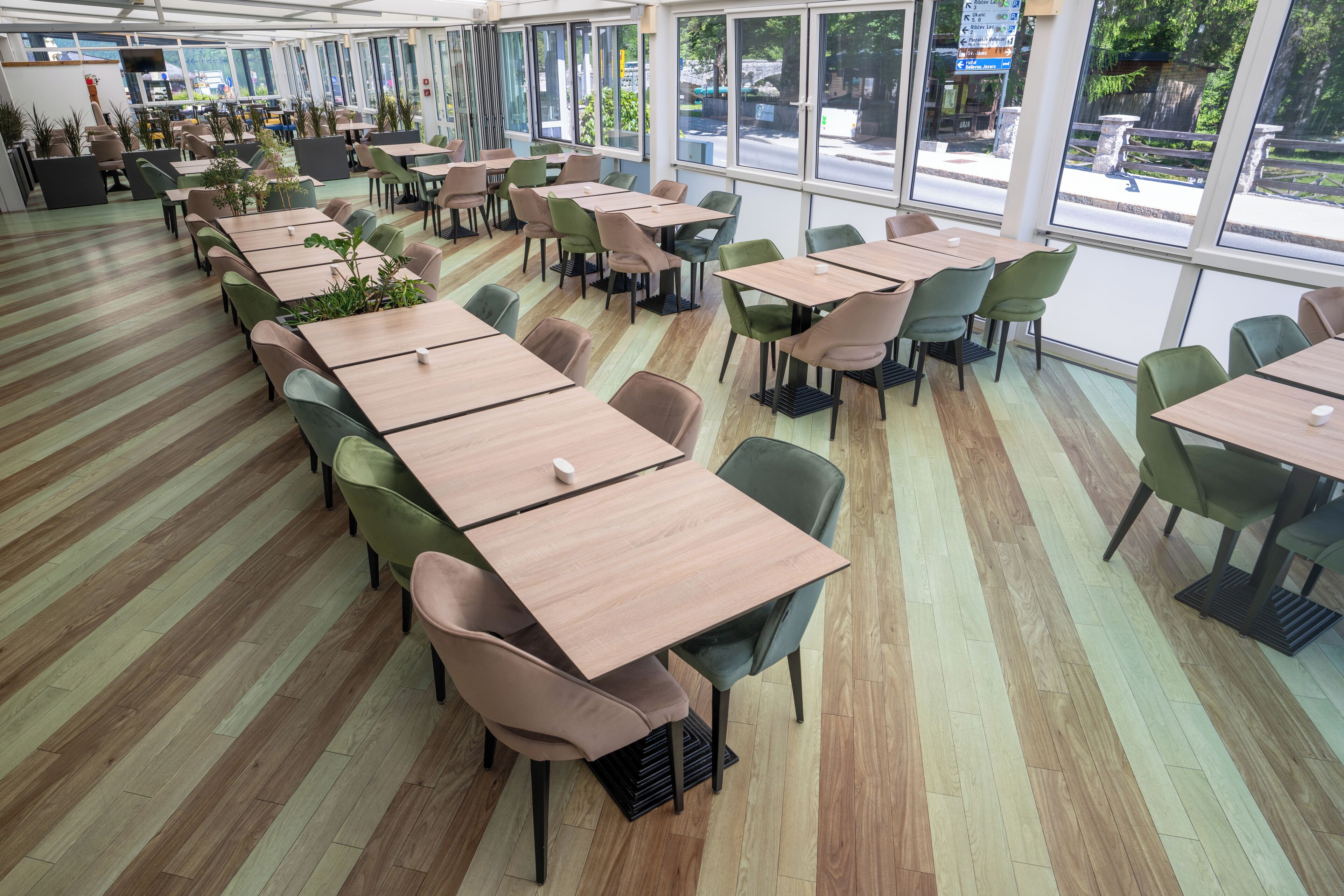 A spacious indoor dining area with multiple tables and chairs, large windows offering views of the street, and a modern, clean design.