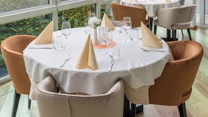 Un restaurante con mesas redondas dispuestas para comer, amplias ventanas que ofrecen vistas a zonas verdes y una carretera, y un interior moderno y cuidado.