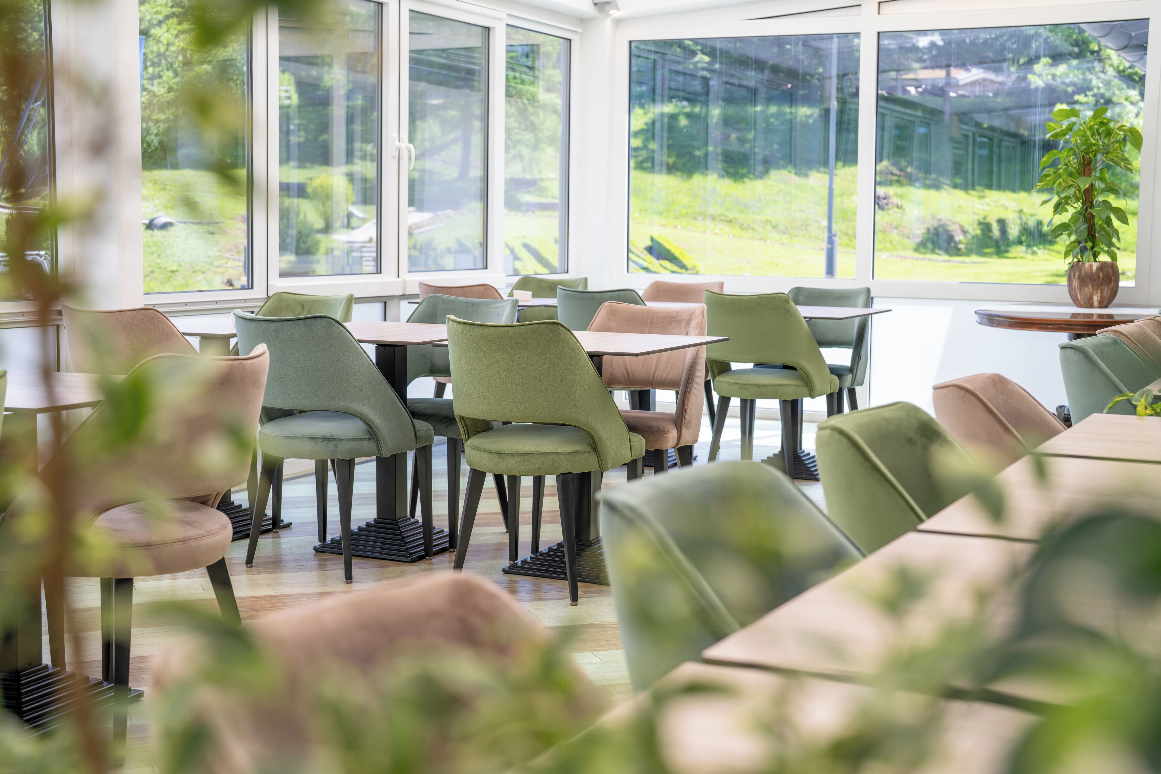 Un espace repas avec des tables et des chaises, de grandes fenêtres et une vue sur la verdure environnante.