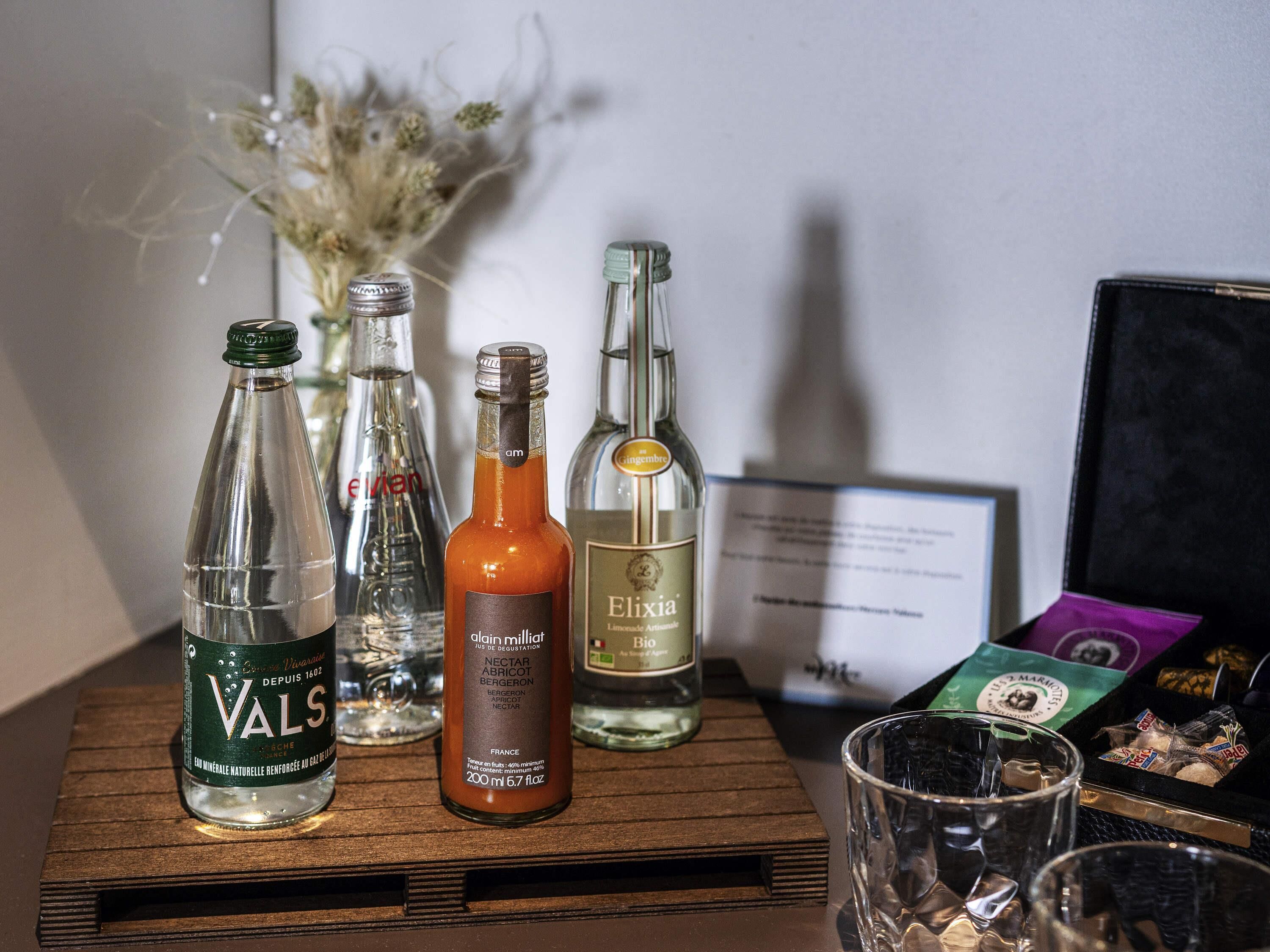 Una bandeja de madera con botellas de Valso, una botella de Elixia y un vaso sobre una mesa.