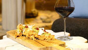 A wooden serving board with a dish and a glass of red wine on a white table.
