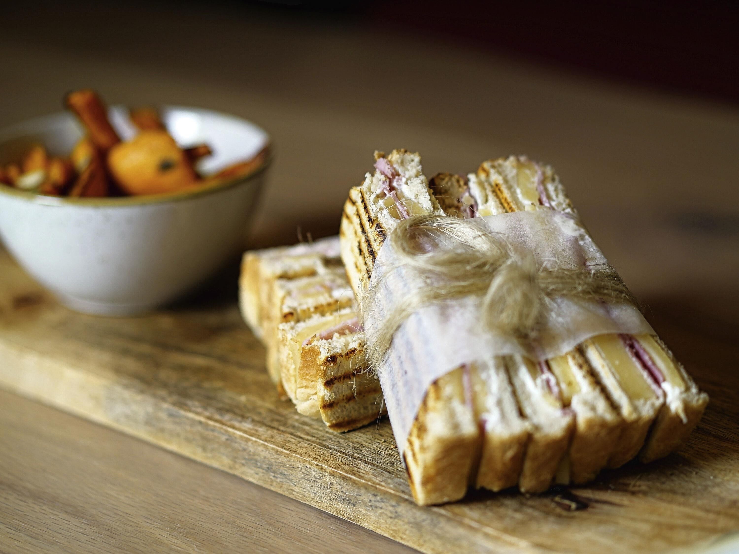 A sandwich wrapped in paper with a string, placed on a wooden board.