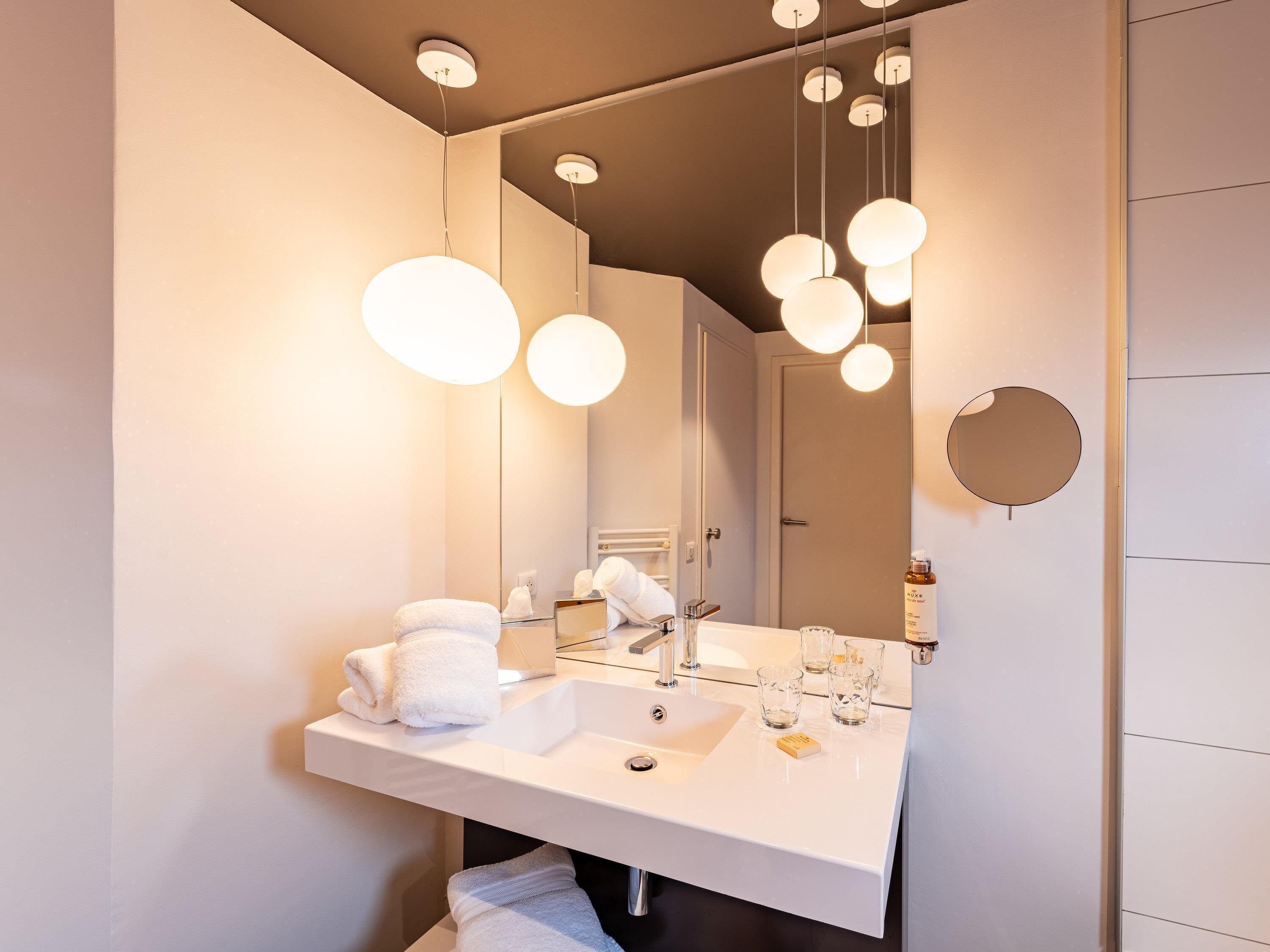A modern bathroom with a large mirror, white sink, and multiple hanging lights.