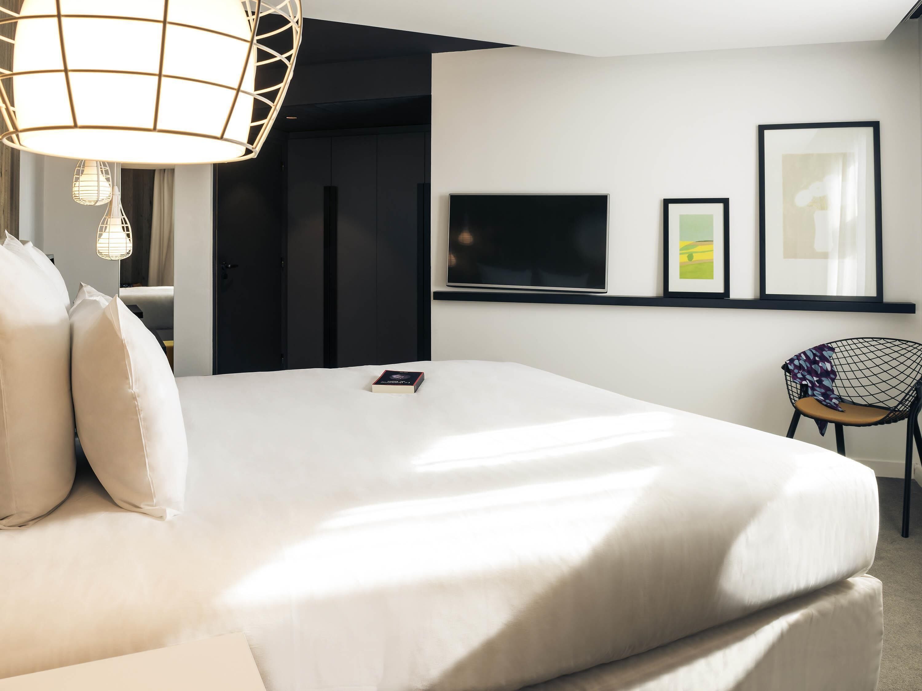 A modern hotel room with a large bed, a television, framed artwork, and a chair.