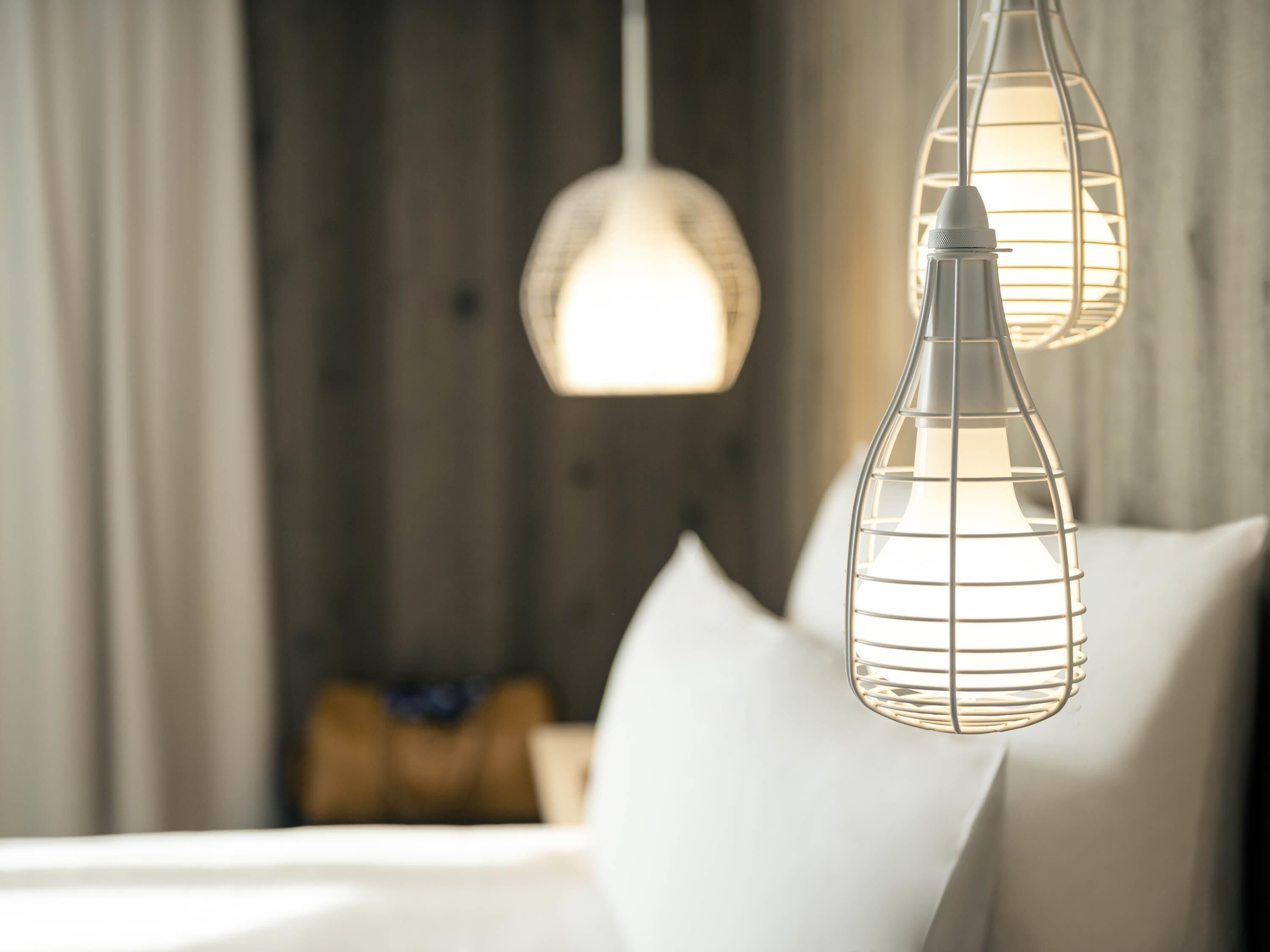 A bed with white bedding and two pendant lights with a wireframe design.