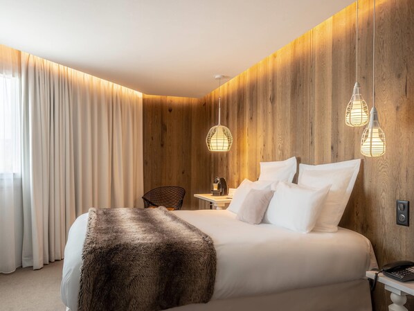 A hotel room with a large bed, wooden panel walls, a desk with a chair, and pendant lights. - Mercure Valence Sud (Valence)