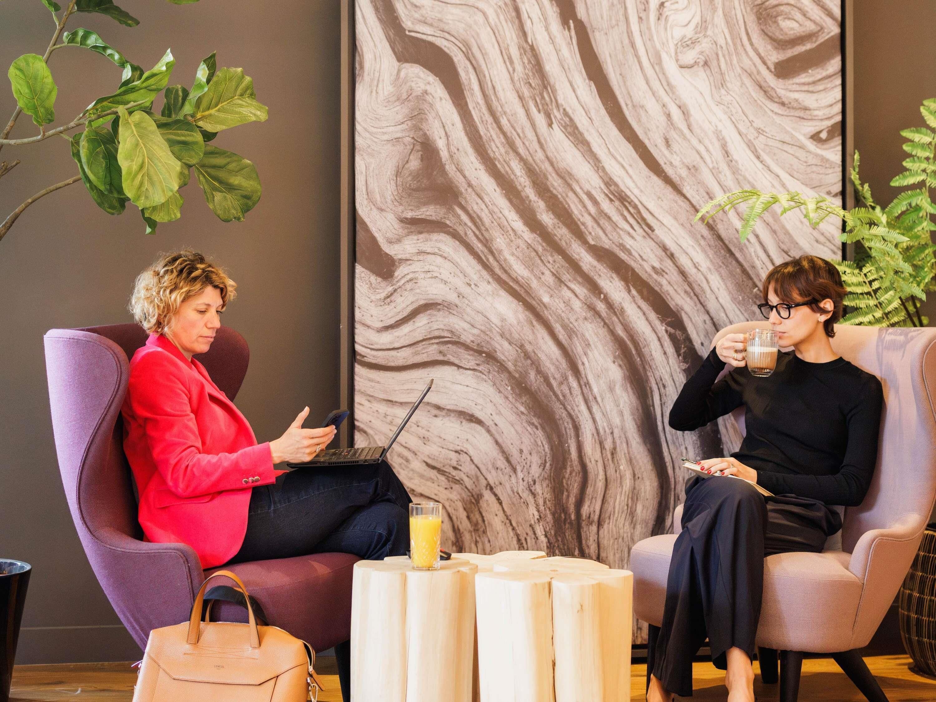 Two people seated in a modern room with a marble wall, a wooden coffee table, and a plant.