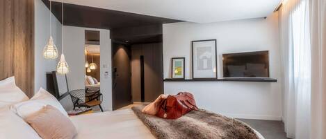 A modern hotel room with a bed, a television, and artwork on the wall.