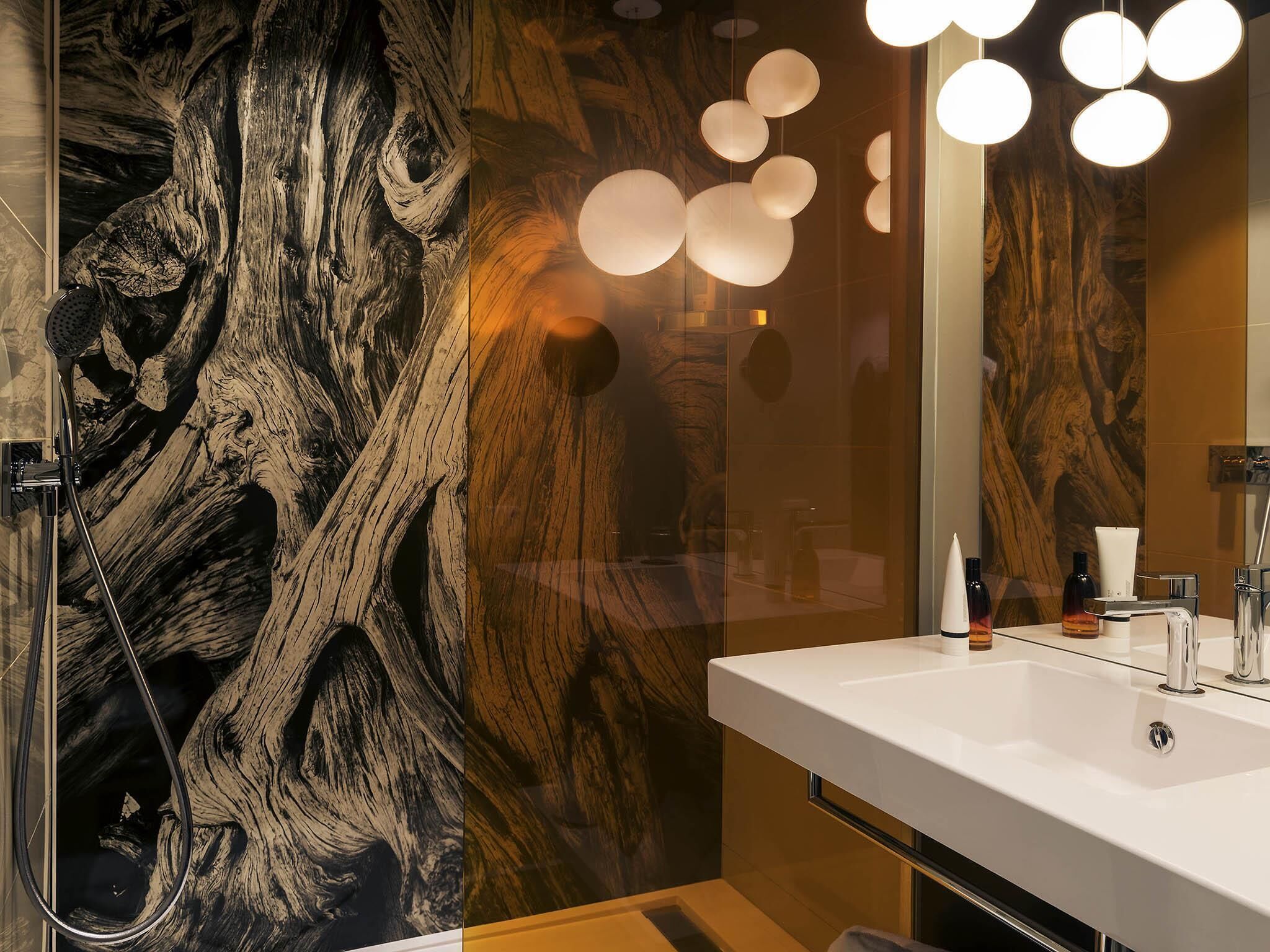 A modern bathroom with a large mirror, a white sink, and a shower with a wooden wall design.