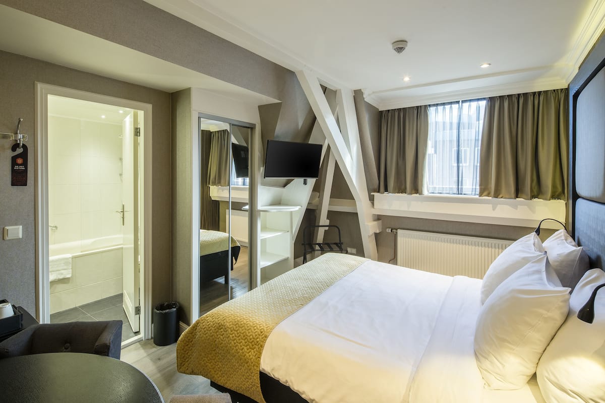 A hotel room with a bed, a TV, a desk, and a bathroom with a shower and toilet.