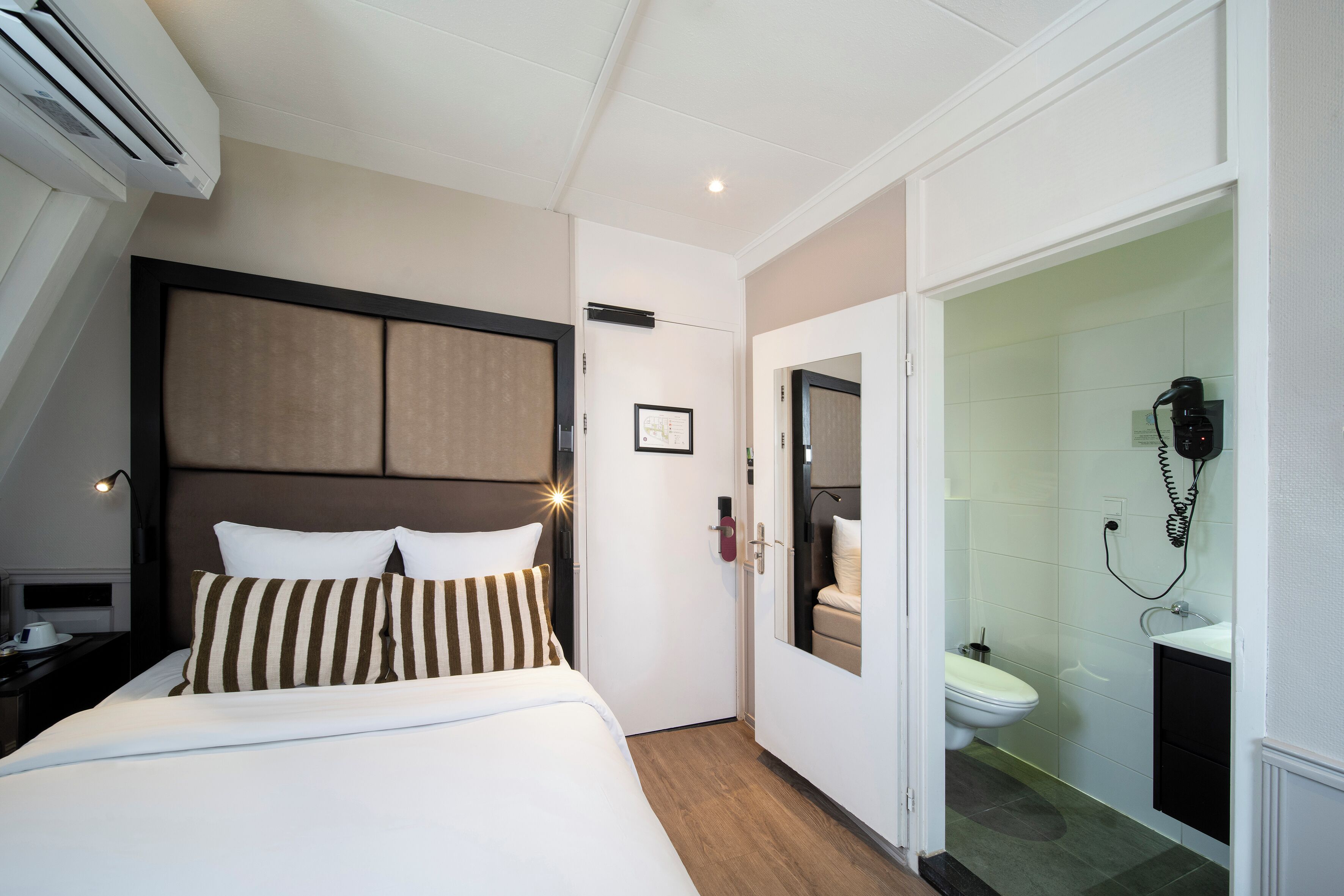 A hotel room with a bed, bedside table, and a bathroom with a toilet and sink.