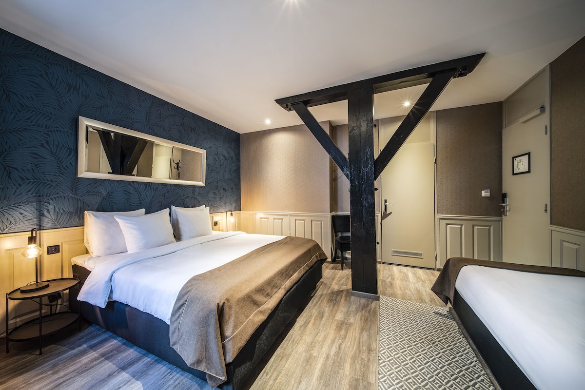 A modern hotel room with a large bed, a smaller bed, a desk, and a wardrobe.