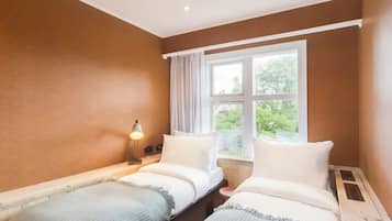 Ein Zimmer mit zwei Betten, einem Fenster mit Vorhängen und einer Nachttischlampe.