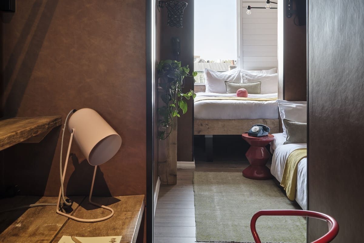 A narrow hallway leading to a bedroom with a bed, a desk with a lamp, a chair, and a telephone.