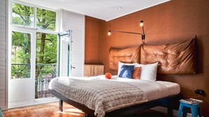 A bedroom with a large bed, a nightstand, a window with a view of greenery, and a wall-mounted lamp. - Max Brown Hotel Museum Square, part of Sircle Collection (Amsterdam)