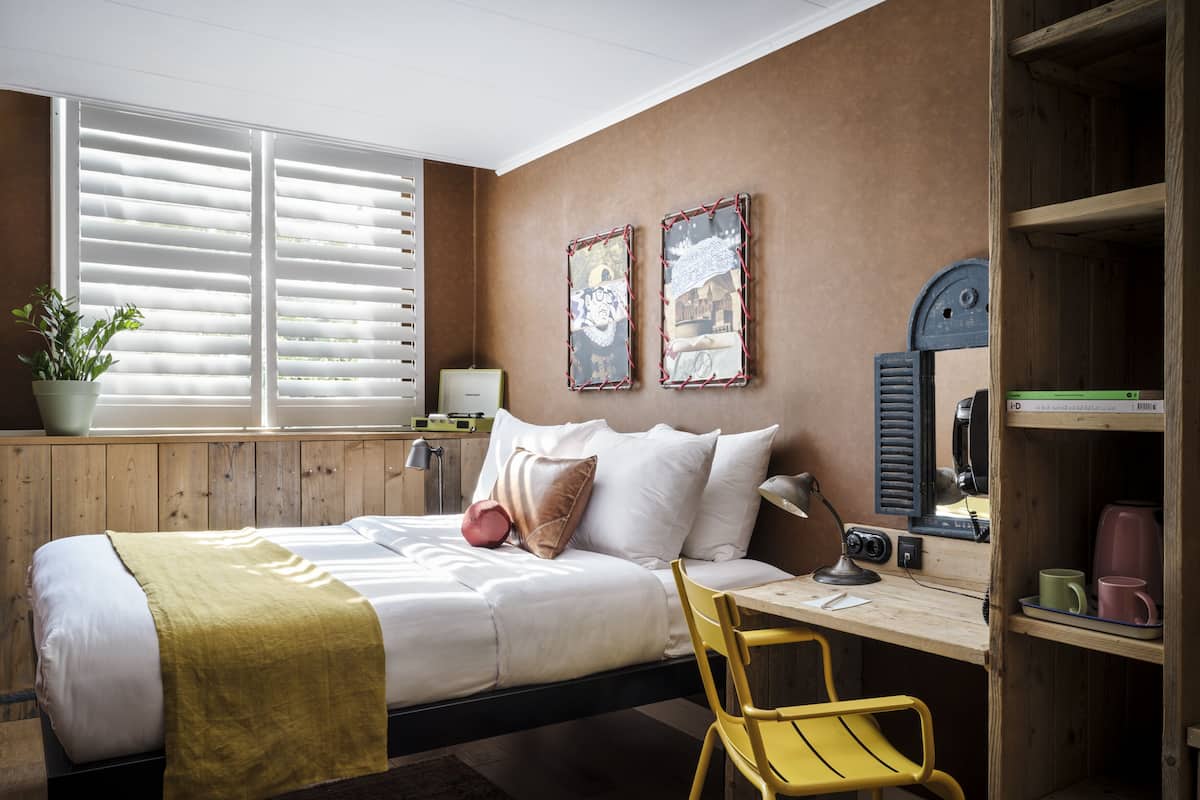 A bedroom with a bed, bedside table, lamp, and a desk with a chair.