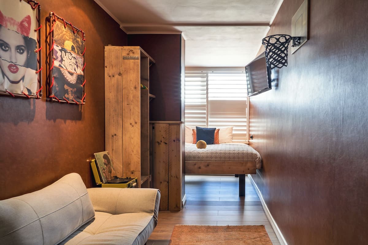 A narrow hallway with a wooden wardrobe, a white sofa, and a bed with orange pillows.