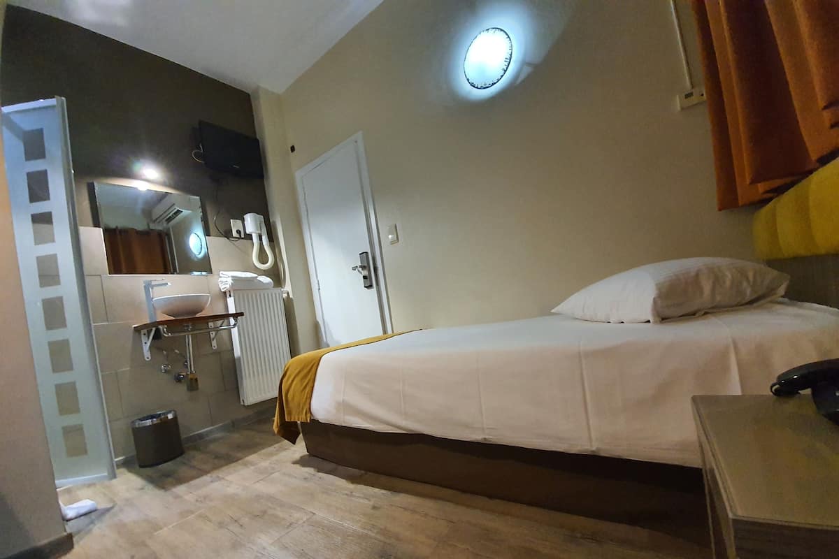 Una habitación de hotel con cama, mesita de noche y baño con lavabo y espejo.