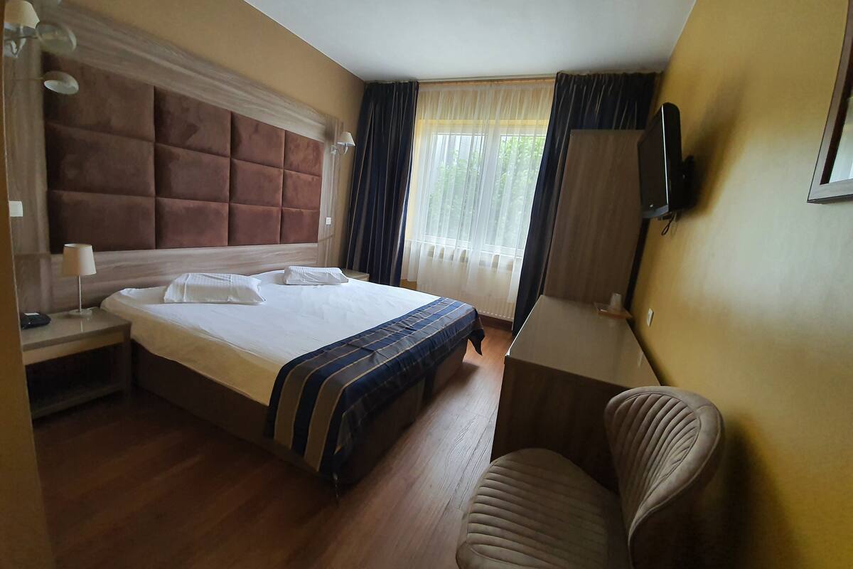 Habitación de hotel con una cama grande, un escritorio, una silla, un televisor y una ventana con cortinas.