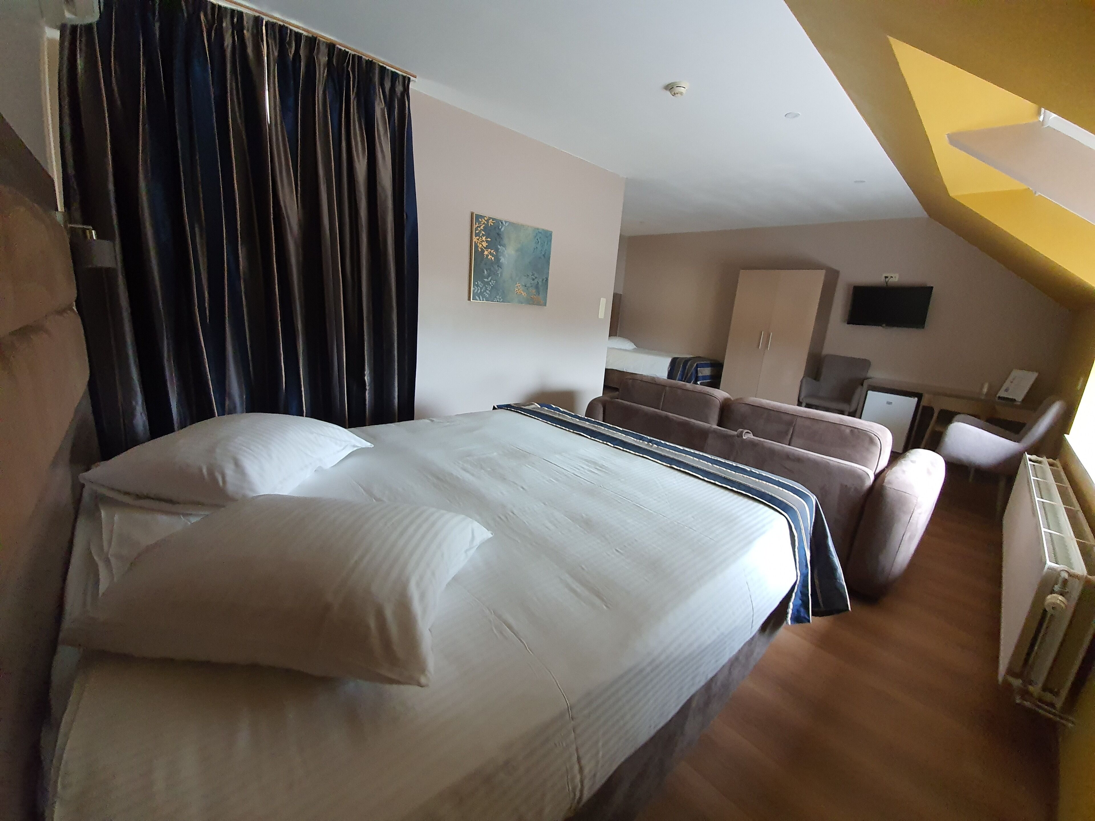 A hotel room with a large bed, a sofa, a TV, and a desk.