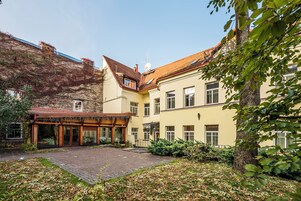 Un cortile con un vialetto in mattoni, una pergola in legno e un edificio con numerose finestre e un tetto rosso.