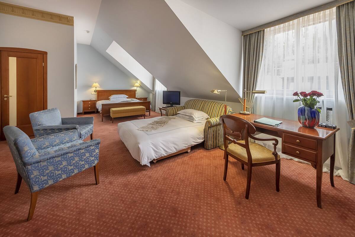 A hotel room with a bed, a desk, a chair, a TV, and a window with curtains.