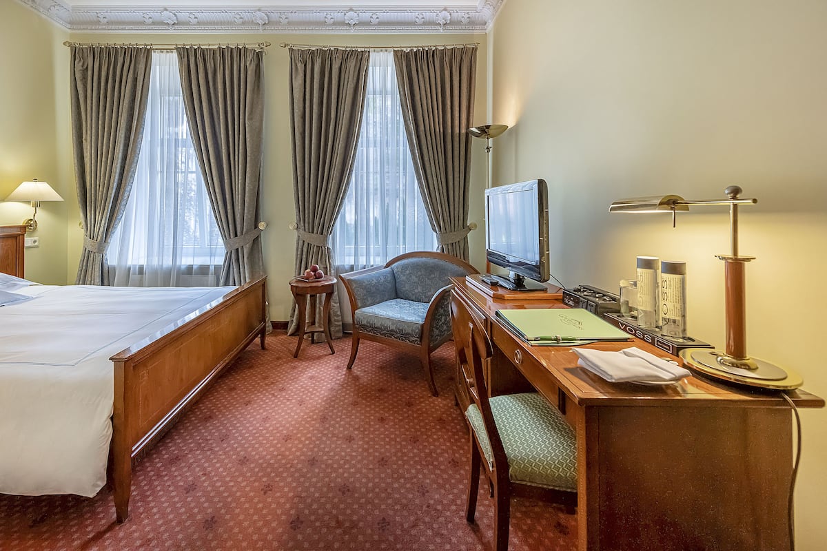 A hotel room with a bed, a desk with a computer, a chair, a lamp, and a television.