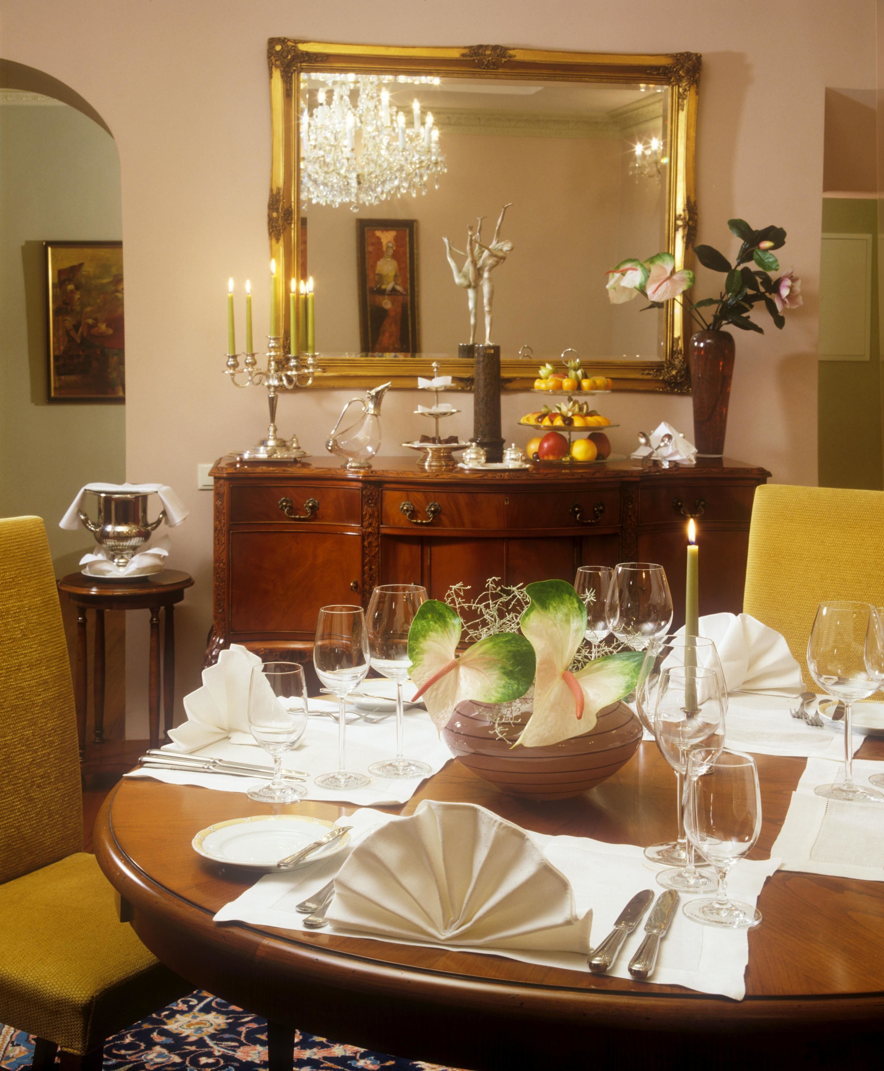 A formal dining room with a wooden table set for a meal, a chandelier, and a mirror above the table.