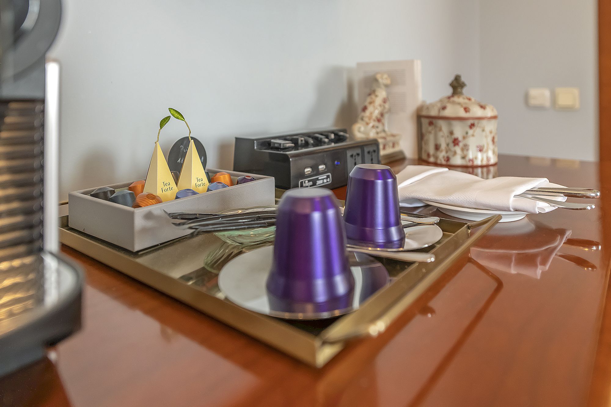 Una bandeja con tazas de té, una caja de bolsitas de té y un pequeño objeto decorativo sobre una mesa de madera.