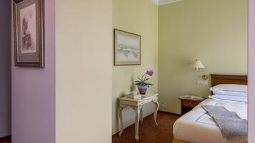 A hotel room with a bed, bedside table with a lamp, a small table with a vase of flowers, and two framed pictures on the wall.