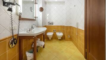 A bathroom with a sink, two bidets, a mirror, and a hairdryer.
