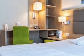 Habitación de hotel con una cama, un escritorio con teléfono, una lámpara, un espejo y una silla verde.