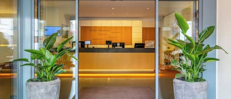 A reception area with a glass door, a reception desk, and two large potted plants.