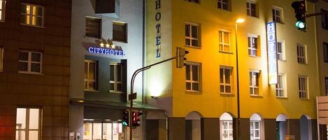 Un hotel con un cartel llamativo que dice 'HOTEL', otro que dice 'CITYHOTEL' y vista de la calle por la noche.