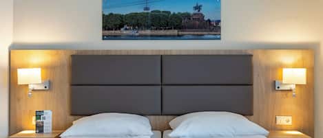 A hotel room with two beds, a large headboard, and a framed picture of a statue and building on the wall.