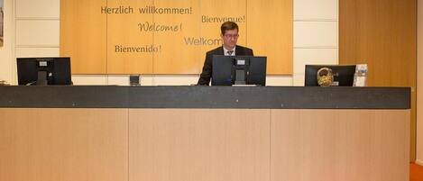A reception desk with a welcome sign in multiple languages and a person seated behind it.