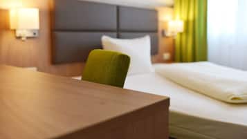 A hotel room with a wooden desk, a green chair, a bed with white bedding, and two wall-mounted lamps.