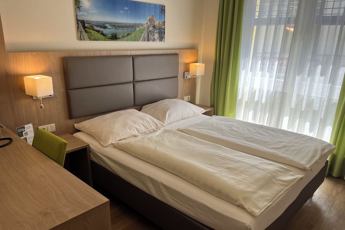 Une chambre d’hôtel avec un grand lit, deux tables de chevet, un bureau et une vue sur le paysage urbain par la fenêtre.