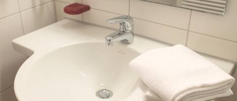 A white bathroom sink with a chrome faucet, a red soap dish, and a white towel on a white countertop.